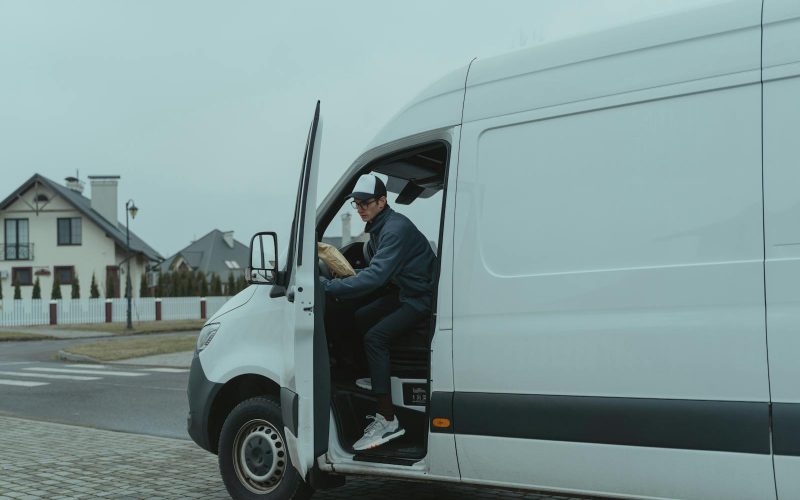 Courier delivering a package from a van in suburban neighborhood, showcasing logistics and last-mile delivery services.